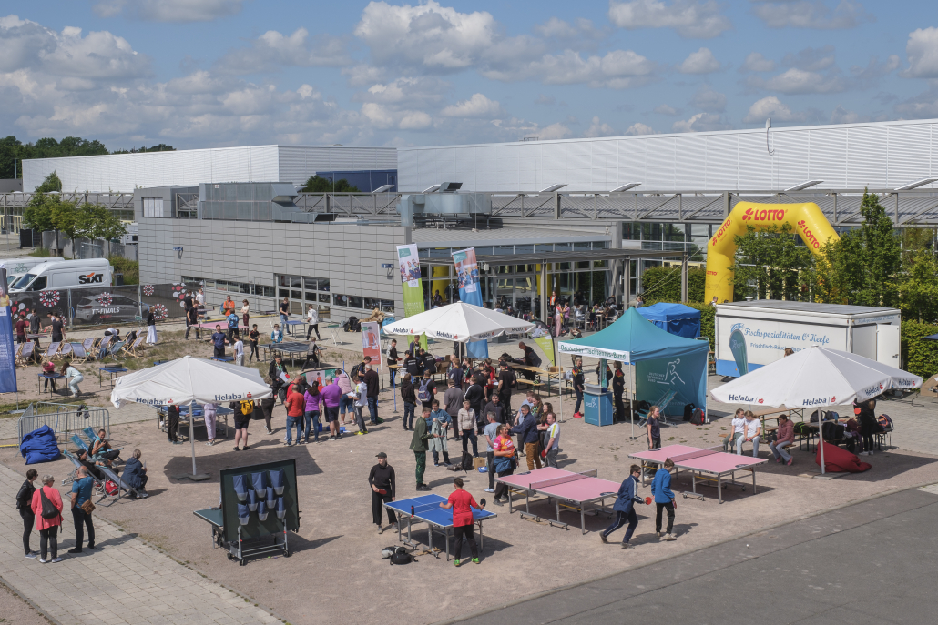Außenbereich der TT-Finals mit vielen Besucher*innen, Aktionsflächen und Tischen.